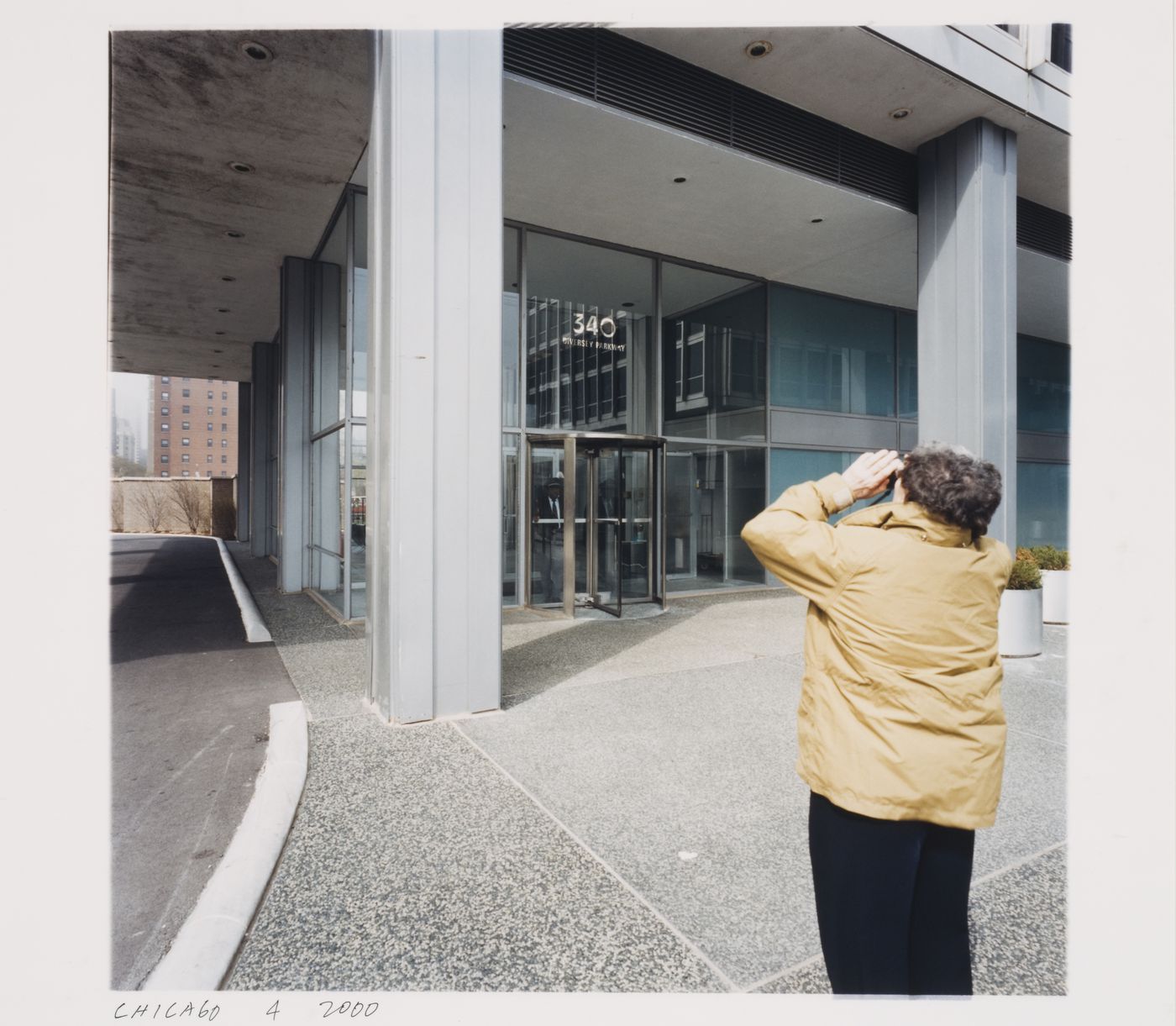 Exterior view looking toward the entrance of 340 Diversey Parkway, showing Phyllis Lambert taking a photograph back turned to the camera, Chicago, Illinois