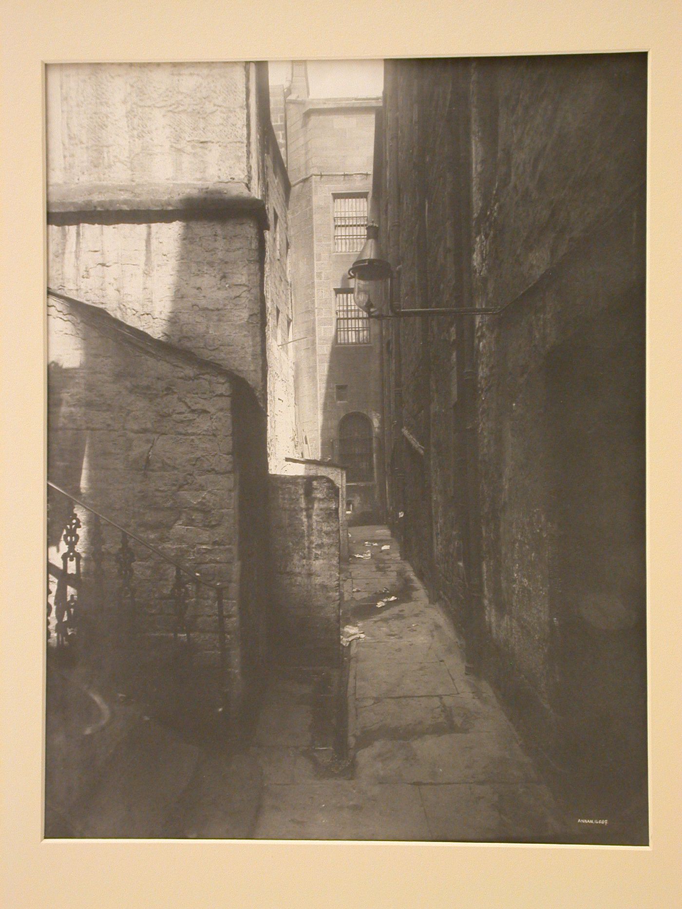 View of an alley with barred windows at the end, stairs at the left, and a gas lantern at the right, Glasgow, Scotland