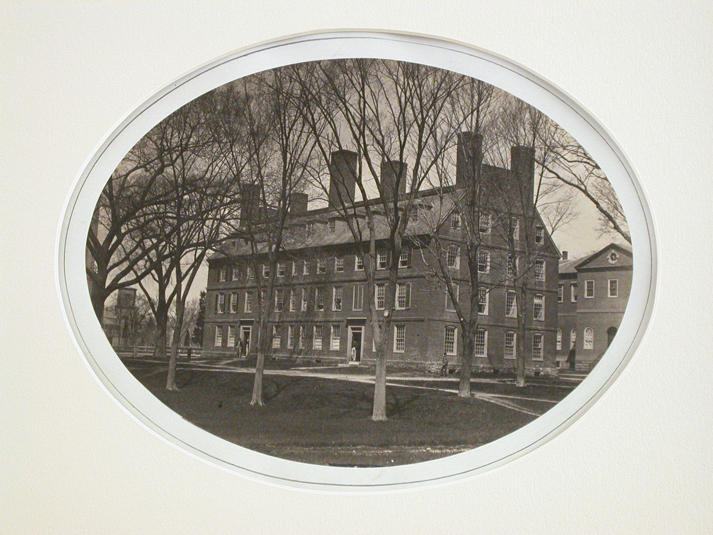 Exterior view of a college building with lawn and trees, figures in doorways, Harvard, Cambridge, Massachusetts