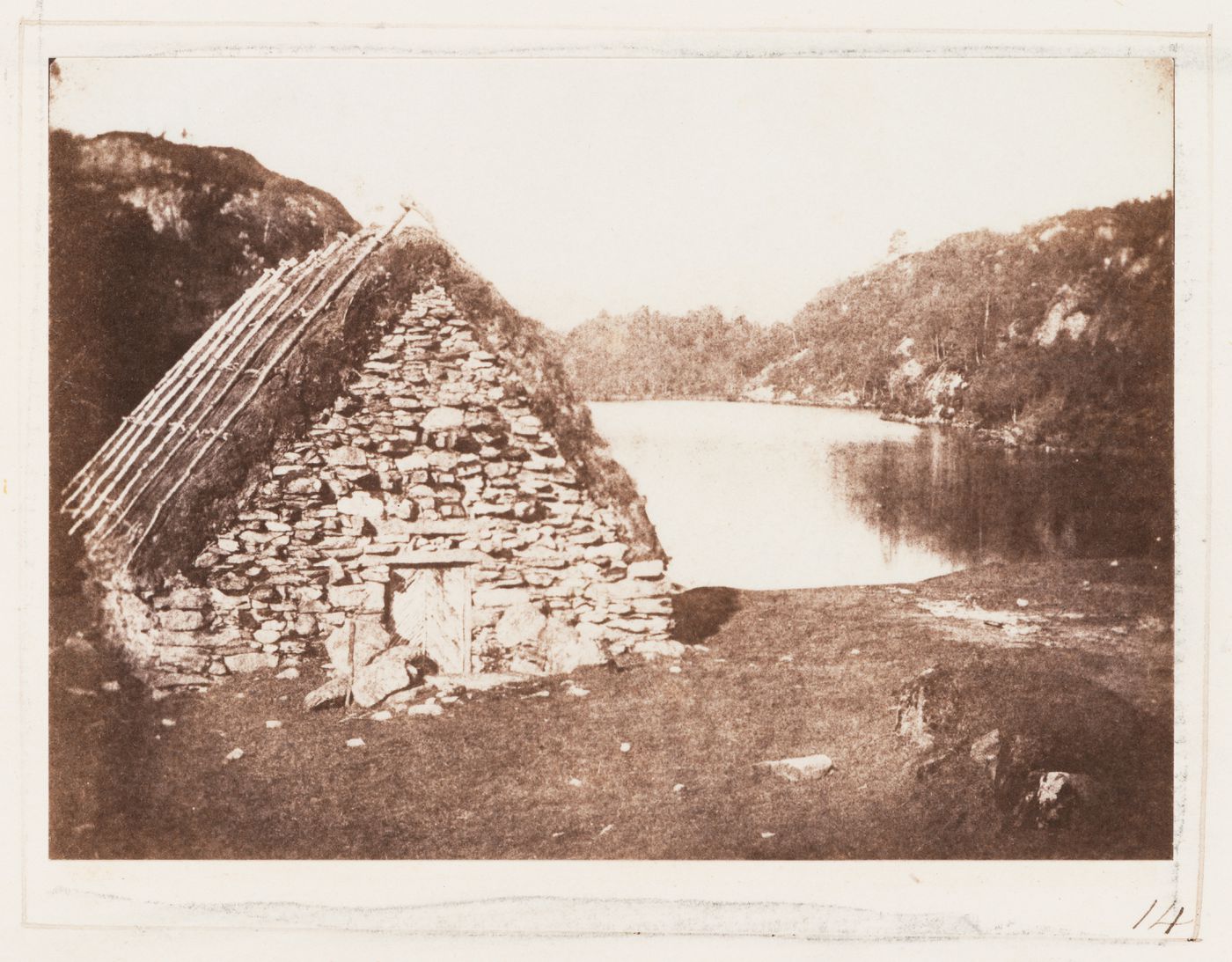View of Highland hut with thatched roof, dry-stacked walls, and wooden door on the banks of Loch Katrine, Scotland