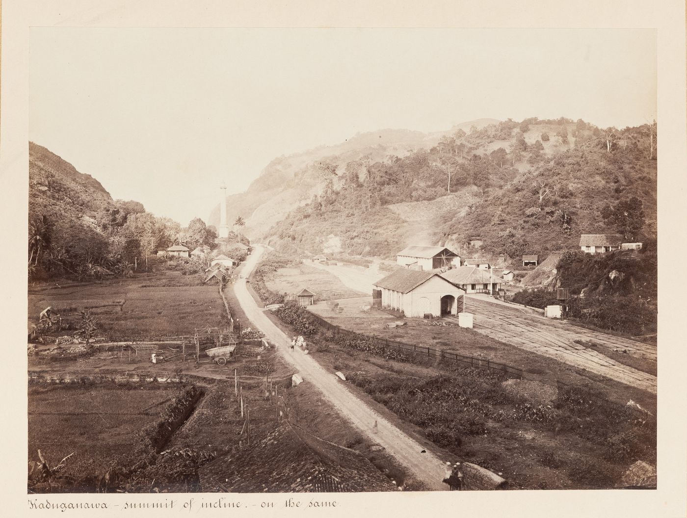 View of Kadugannawa showing a road and hills with the railroad station on the right and Captain Dawson's Monument in the background, Ceylon (now Sri Lanka)