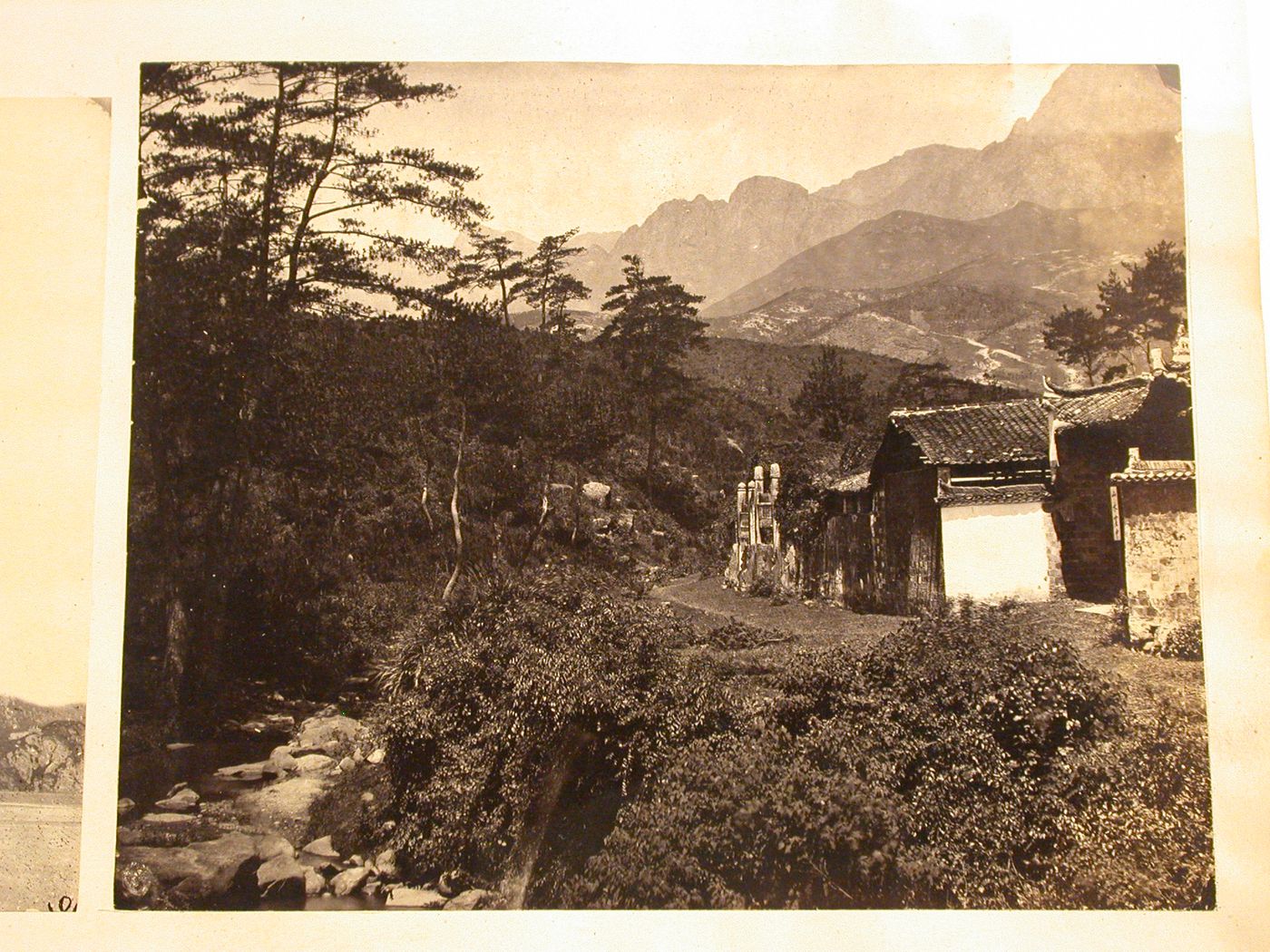 View of a river on the left and dwellings along a road on the right with mountains in the background, China