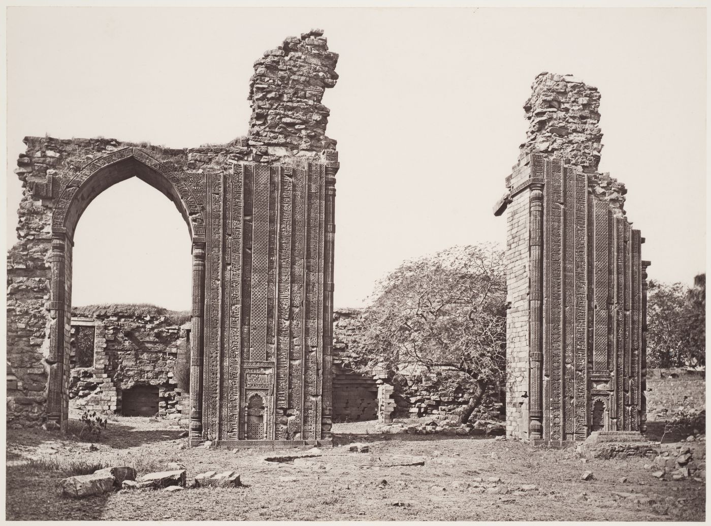 View of the north-west gateway and the arched screen façade of the Quwwat al-Islam [Might of Islam] Mosque with an unidentified building in the background, Quwwat al-Islam Mosque Complex, Delhi, India