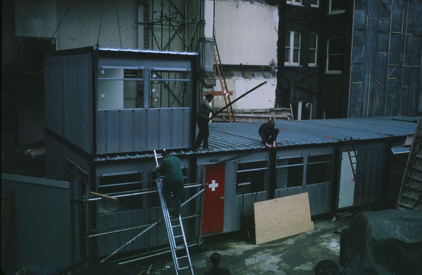 McAppy: view of workers assembling portable enclosures, including a First Aid station, at the Angel Court site