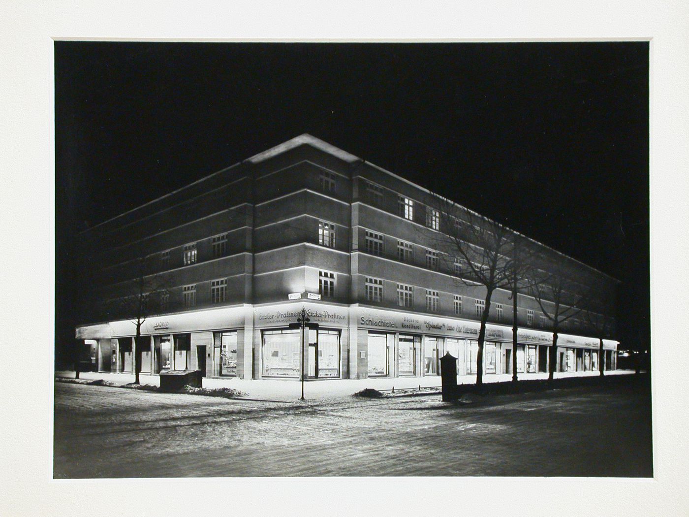 Illuminated night view of four-story modern building on a street corner, Germany