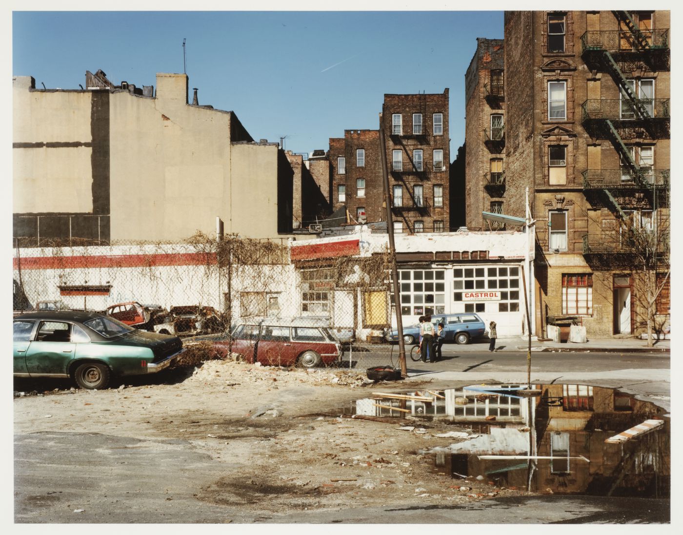 View of parking lot, gas station across street, children in street, New York City, New York