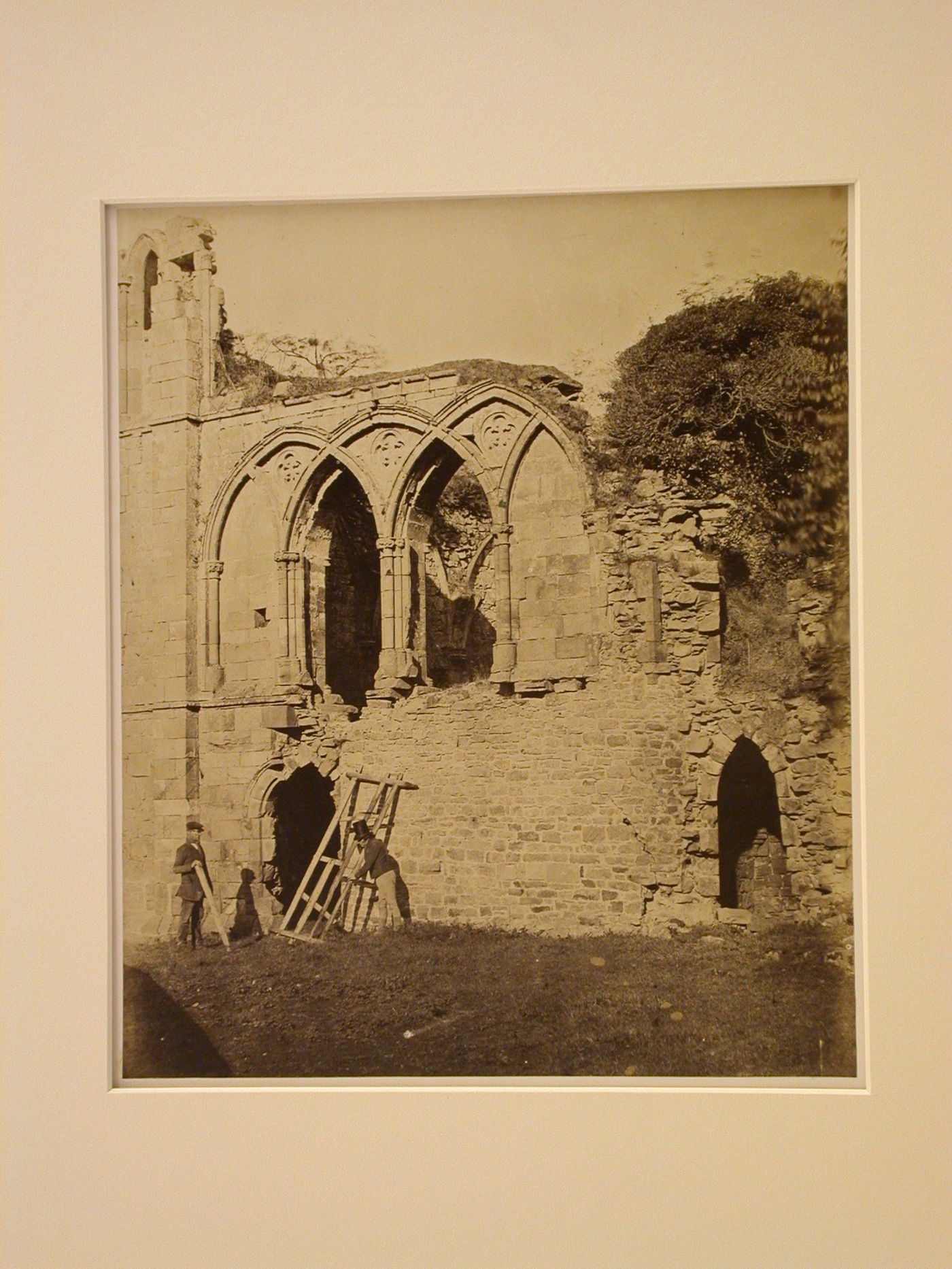 Partial view of Easby Abbey showing the ruins of the guest chamber and two men moving a piece of fence, near Richmond, North Yorkshire, England