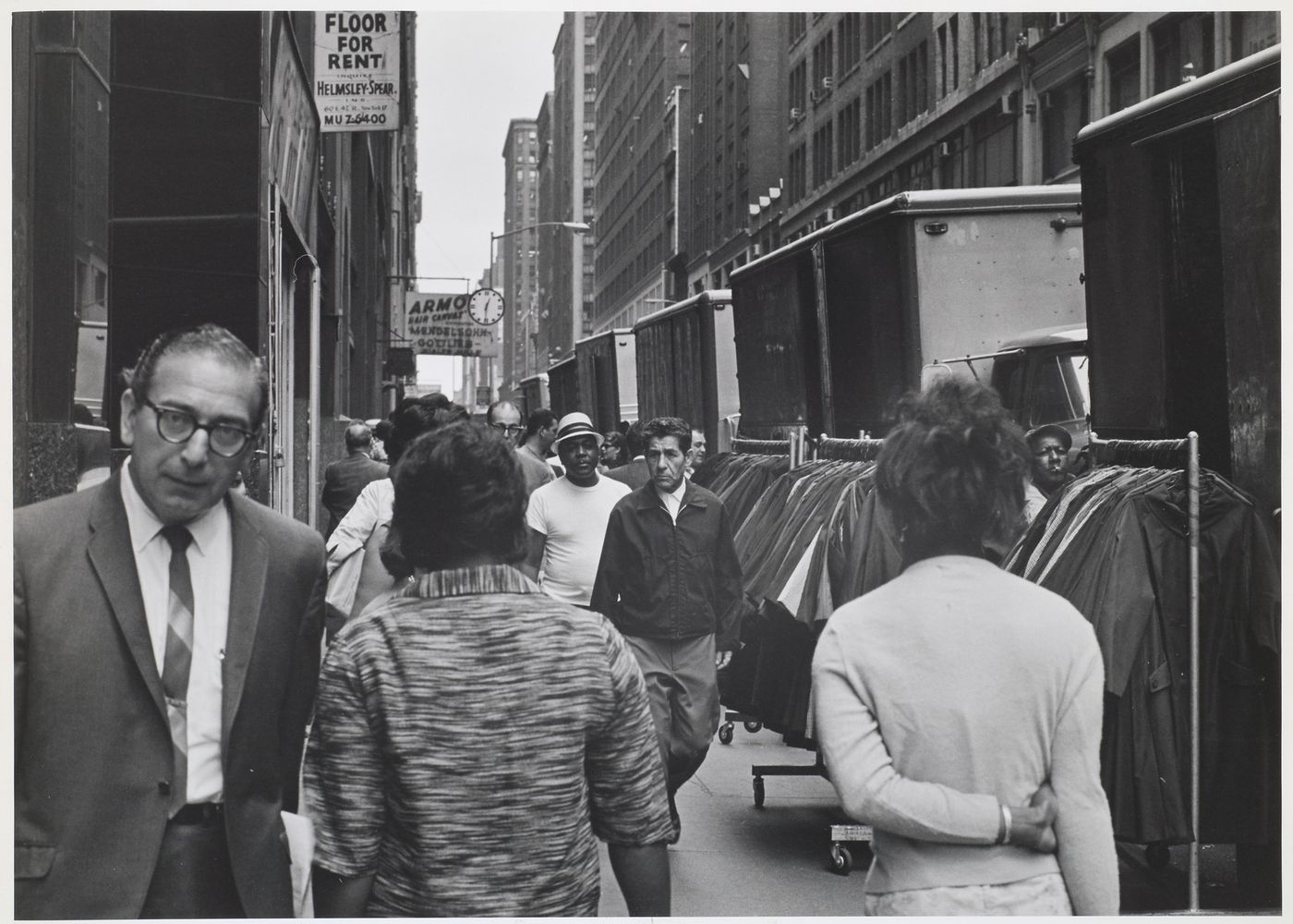 Group portrait of pedestrians showing rolling garment racks, trucks and buildings, West 37th Street, Manhattan, New York City, New York