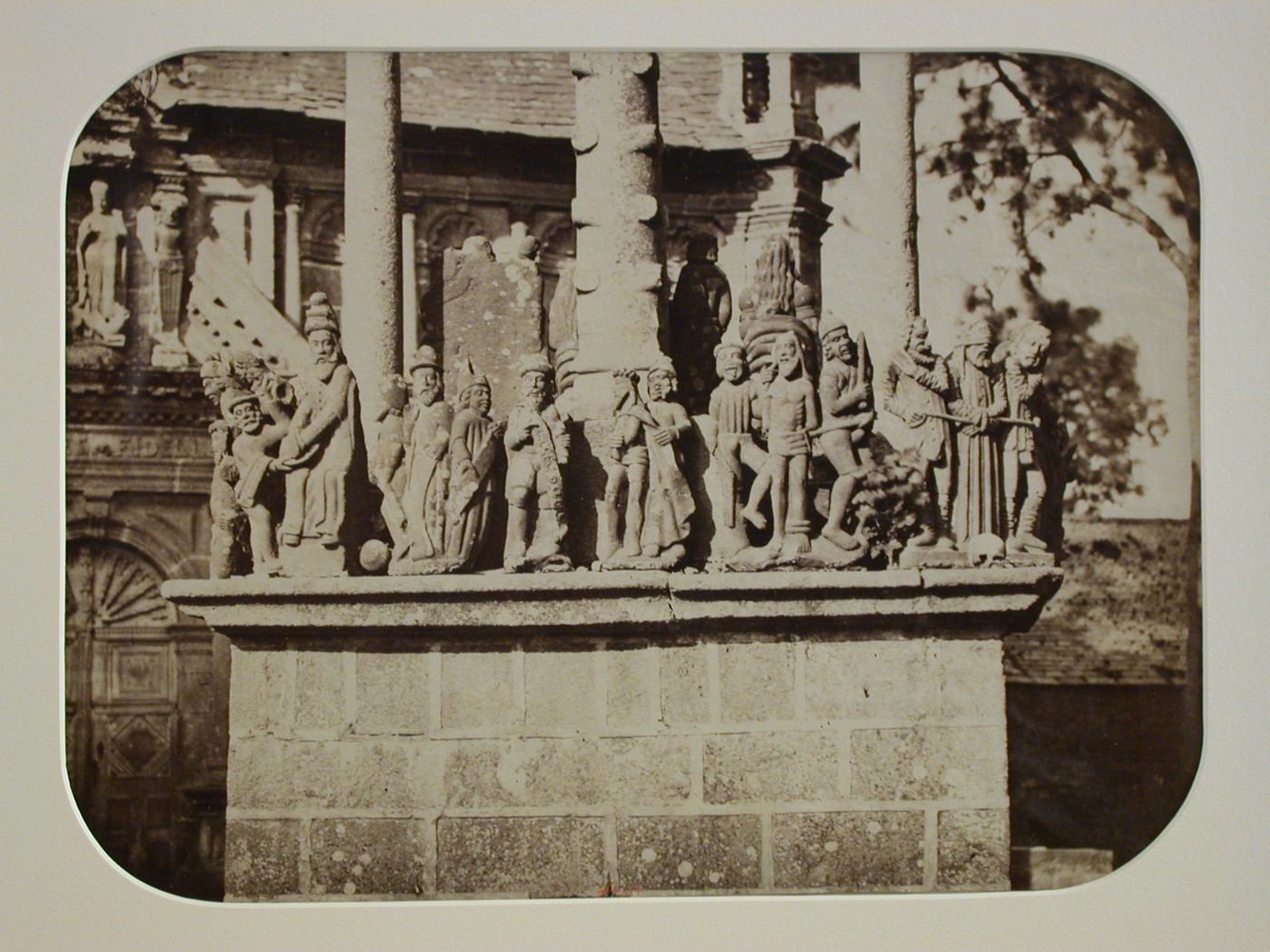 Detail of base and lower portion of Calvary with church in background, Saint-Thégonnec, France