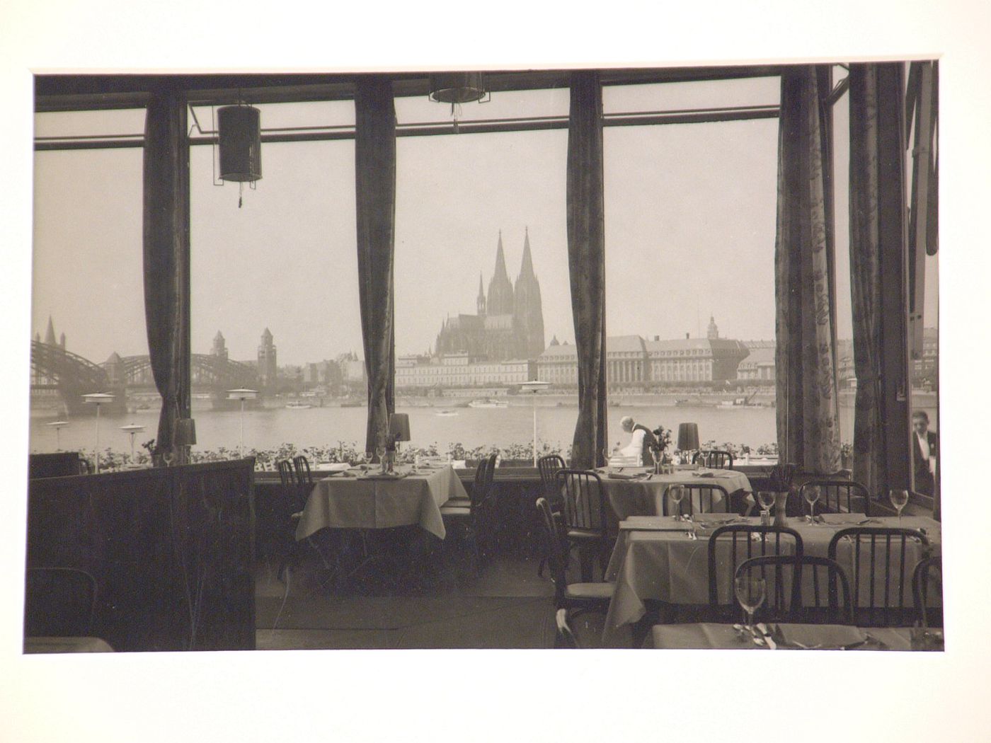 Interior of riverside restaurant with view through large windows of bridge, river and Cathedral, Cologne, Germany