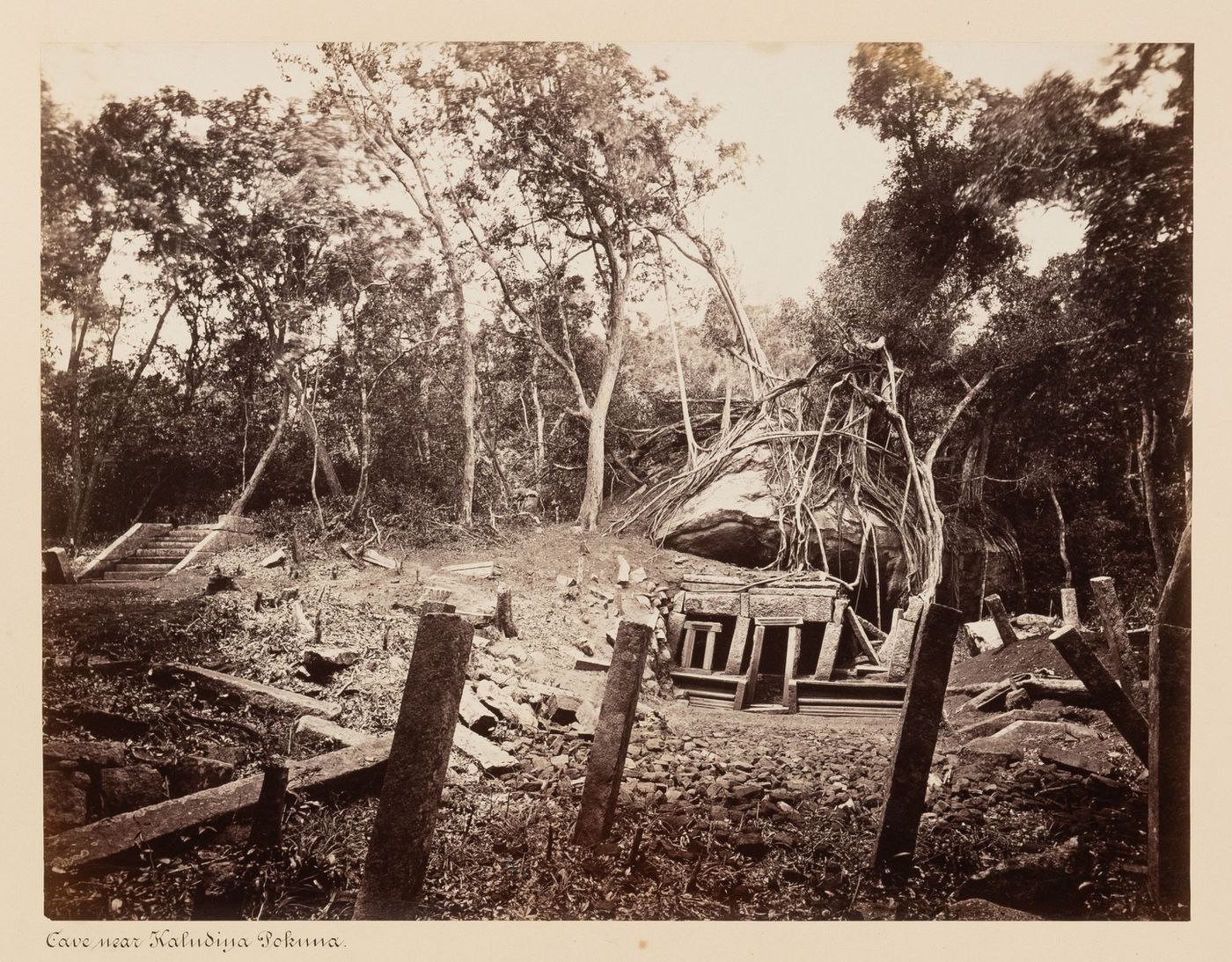 View of a cave temple [?] with a staircase on the left and ruins in the foreground, near the Kaludiya Pokuna [bathing pool], Mihintale, Ceylon (now Sri Lanka)
